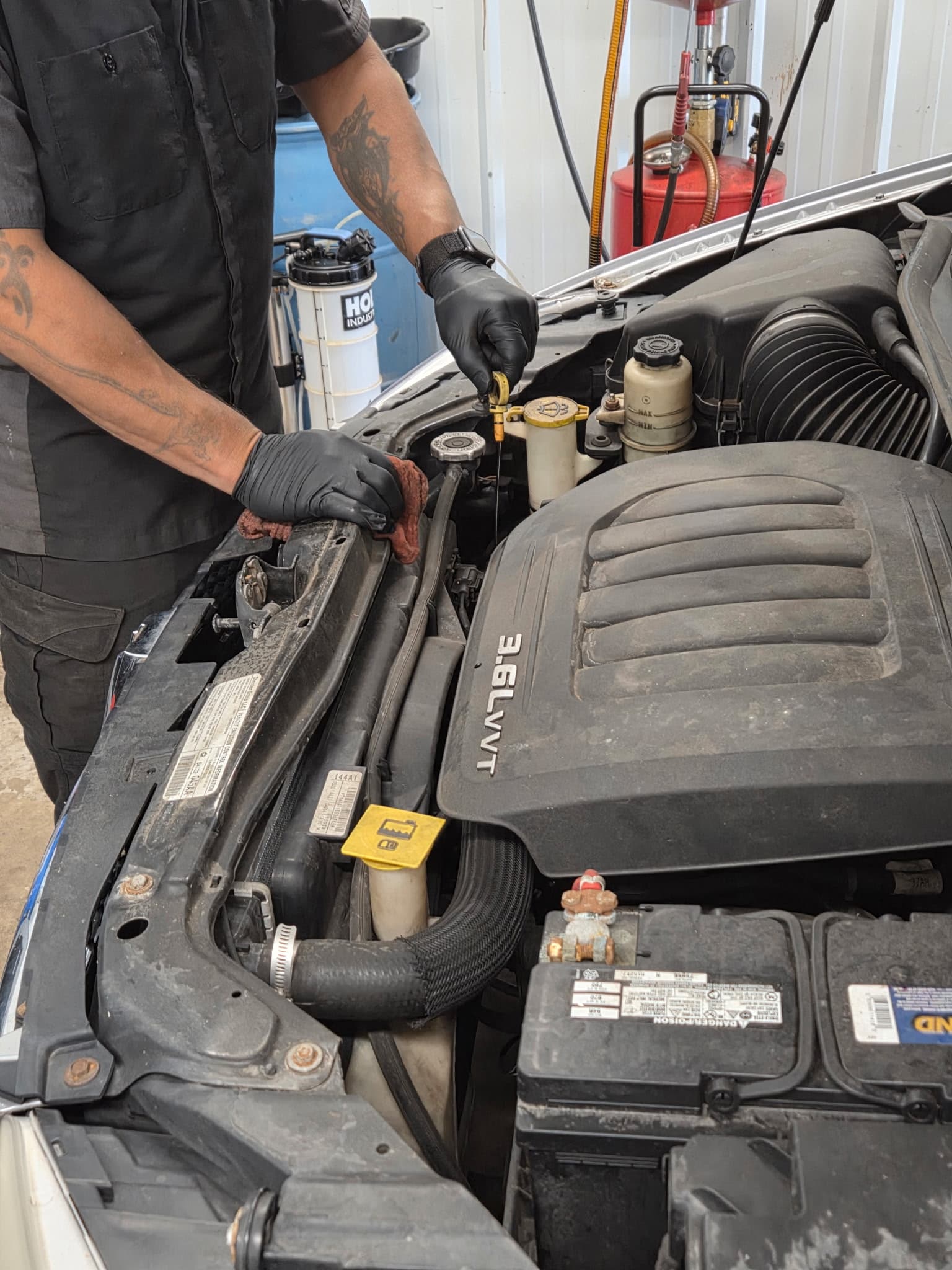 Mechanic wearing black gloves pulls an oil dipstick from a vehicle's 3.6L VVT engine.